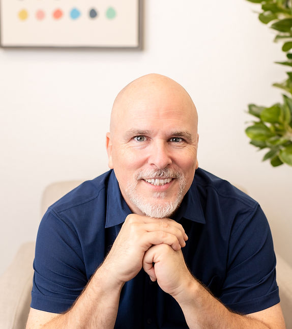 Kirk Stafford, LCSW, LCDC, smiling lead therapist at Canvas Outpatient, seated in a welcoming therapy space with a plant and colorful artwork in the background.